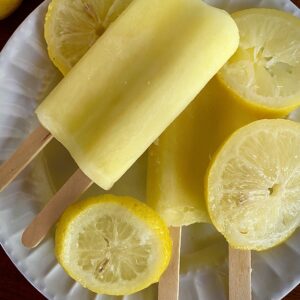 Lemon popsicles on white plate with lemon slices.