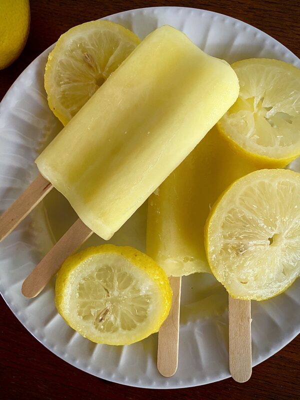 Lemon popsicles on white plate with lemon slices.