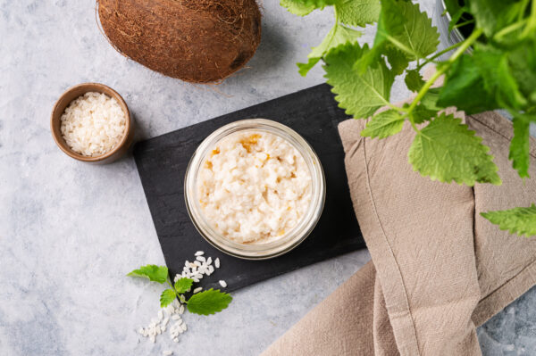 Rice porridge with coconut milk and mango slices in a jar on a light background.