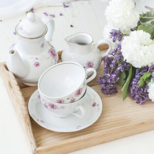 White tea set, a bouquet of lilac in a vase and a sprig of lilac in a cup