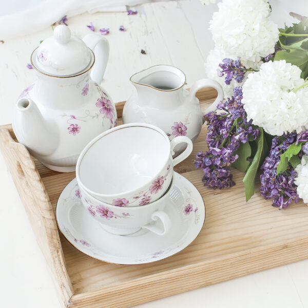 White tea set, a bouquet of lilac in a vase and a sprig of lilac in a cup
